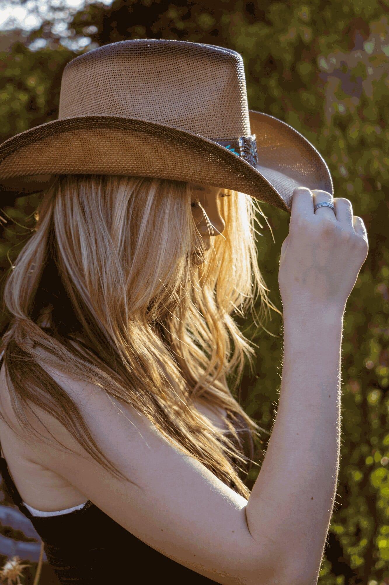 Young woman tipping a straw cowboy hat over her face in backlit golden hour light — Sacramento senior portrait photographer