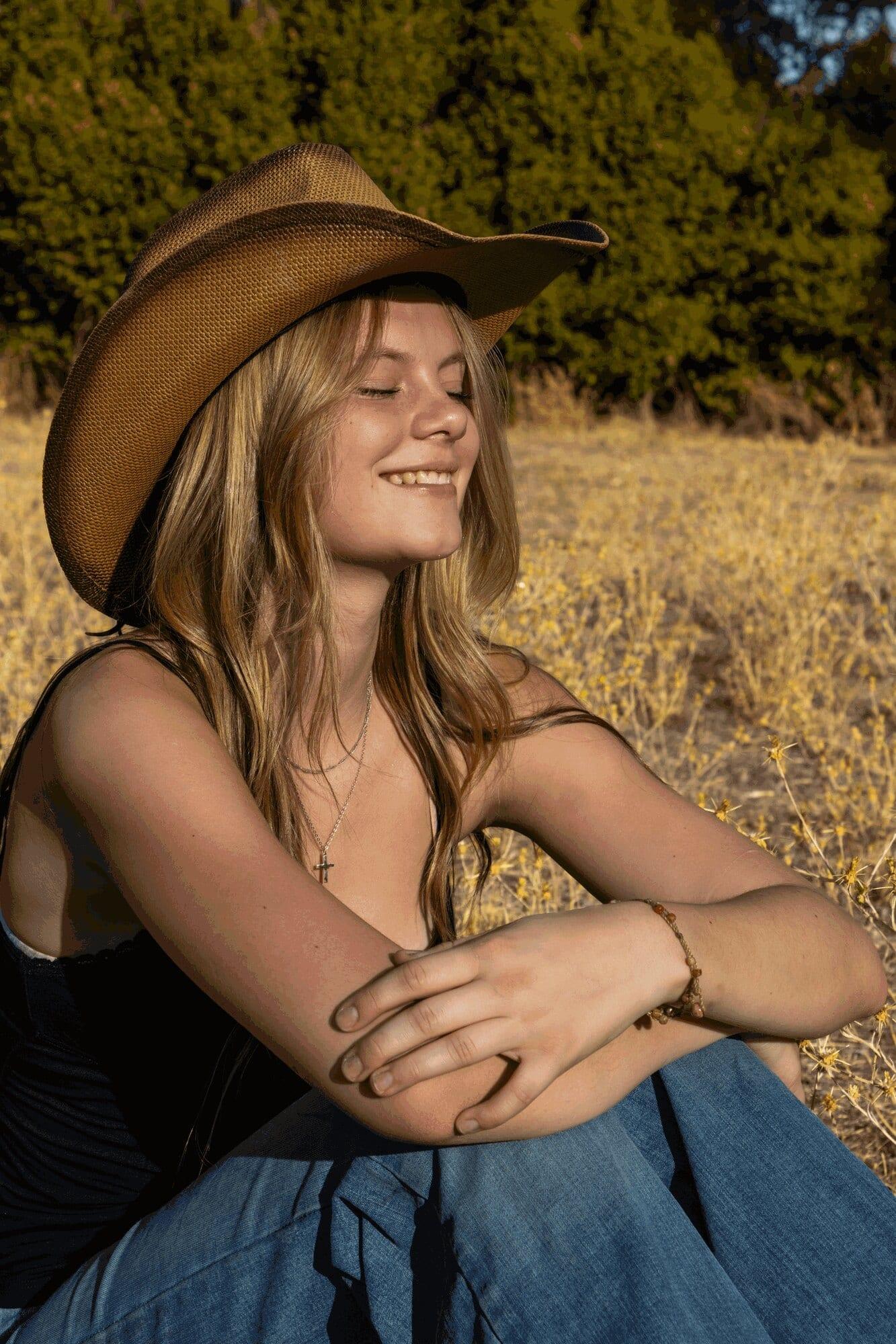 Senior girl in a cowboy hat smiling with eyes closed in a dry golden field — Sacramento senior portrait photographer